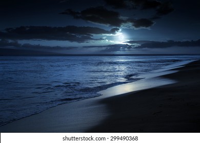 This photo illustration depicts a quiet and romantic moonlit beach in Maui Hawaii. It could represent any beach at night with calm waves and cloud filled night time sky. - Powered by Shutterstock