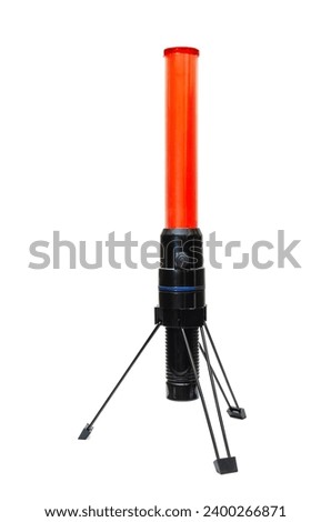 This is a photo of a red and black road baton. The baton stands vertically on a tripod. It is cylindrical in shape with a red top and a black base. The baton has a button on the side.  The background 
