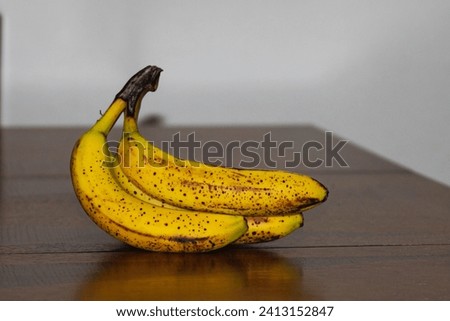 This is a photo shot of a ripe banana bunch with dark spots on table. 