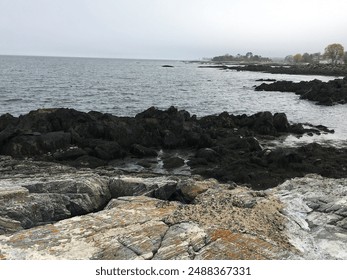 This photo shows a coastal scene in New Hampshire, featuring a rocky shoreline extending into a calm body of water. The foreground is dominated by large, jagged rocks with varying shades of gray, some - Powered by Shutterstock