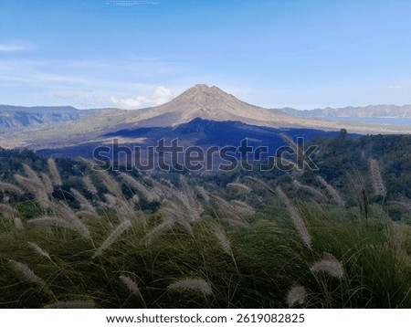 This photo shows a dramatic view of Mount Batur towering over the Kintamani area of ​​Bali. The active volcano dominates the landscape with its distinctive cone shape and vast surrounding caldera area