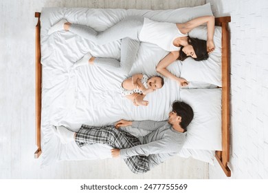 This photo shows a family of three sleeping in a bed together. The parents are on the outside of the bed, while the child is in the middle, top view - Powered by Shutterstock