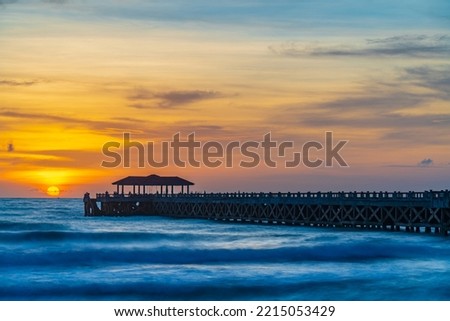 This is the photo of sunset at pier in Thailand. The location is Had Natai beach in Pang-nga. Some people are waiting to see sunset and some fishermen are catching fish.