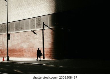 This photograph captures the ambiance of warm light and harsh shadows as a lone figure walks in the distance. The scene is characterized by the golden hues of the light, casting long and dramatic shad