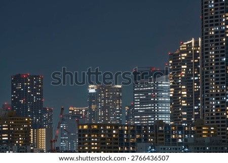  This photograph captures the overlapping of multiple skyscrapers with different designs, utilizing a compression effect. The contrast between the organic curves of the cylindrical building on the left and the linear grids of the building on the right highlights the complex structural beauty of the city. The white and yellow lights leaking from countless windows each symbolize the lives of the people working or living there, giving the massive structures a sense of human warmth.    