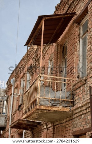 This photograph captures a section of a brick residential building in Tbilisi, featuring a weathered metal balcony. The rusted railing and simple design reflect the city’s architectural heritage and the passage of time.