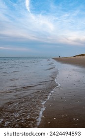 This photograph captures the vastness of an open beach under a spacious sky, where the elements of earth, water, and air converge. The beach stretches into the distance, with the shoreline delineated
