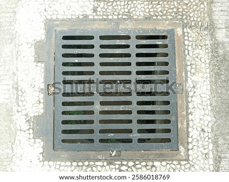 This photograph features a rectangular metal drain cover, clearly marked with 