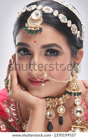 This photograph showcases a stunning Indian bride adorned in traditional attire, radiating grace and elegance while posing for a picture. The bride’s ensemble includes ornate jewelry, makeup