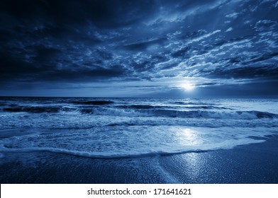 This is a photographic illustration of a beautiful midnight blue ocean moonrise along the coast with dramatic sky and rolling waves. - Powered by Shutterstock