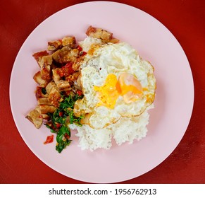 this pic show the crispy pork with Thai basil and egg fried on rice, with red table background it's a classic Thai dish.