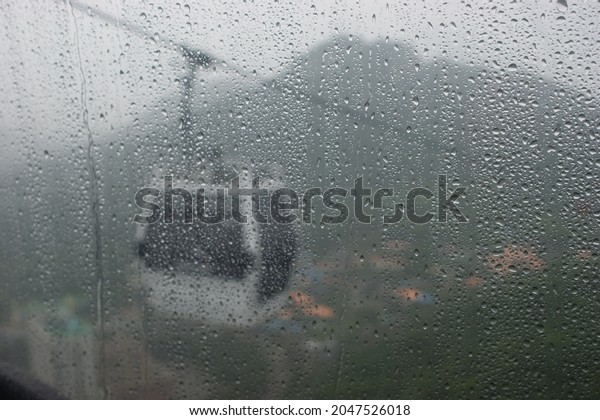 This is a picture of a window surrounded by\
raindrops in a cable car on a rainy\
day.