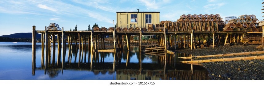 This is a pier with a small square wooden shack. There are lobster traps stacked up on the pier.