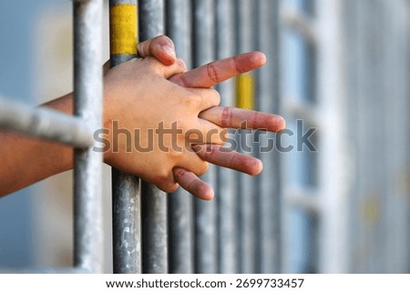 This powerful image captures hands gripping metal bars, symbolizing confinement and restriction. It evokes emotions of sorrow, struggle, and hope amidst a backdrop of isolation.