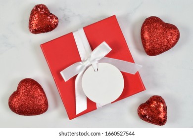 This Present Mock Up Features A Red Present Topped With White Ribbon And A Round Gift Tag. The Gift Is Surrounded By Glittery Red Hearts. 