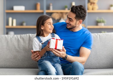 This Present Is For You. Portrait of loving girl sitting on dad's lap and greeting him with father's day or birthday, holding wrapped gift box, happy family celebrating holiday together at home - Shutterstock ID 1959191692