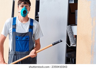 This is professional painter in respirator and goggles with paint roller in his hands. Portrait of genuine working man. Painter looks into camera. - Powered by Shutterstock