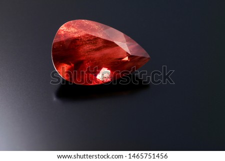 This red orange colored pear cut sunstone sits on a black reflective background and shows strong shilling.