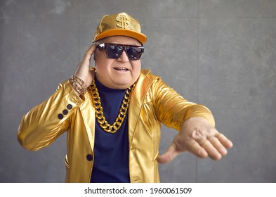 This Is The Rhythm Of My Life. Funny Rich Senior Man Playing Music At Disco Party. Studio Portrait Of Happy Old Guy In Golden Jacket, Baseball Cap And Gold Chain Necklace Mixing Songs On DJ Turntable