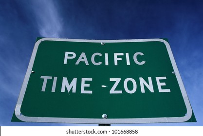 This Is A Road Sign Indicating A Change To The Pacific Time Zone. The Sign Is Green Against A Blue Sky.