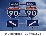 This is a road sign on the New York State Freeway. It points out the direction for Route 90 to go east or west. The signs are blue, red and white against a blue sky.