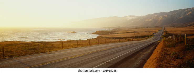 This is Route 1, also known as the Pacific Coast Highway. The road is situated next to the ocean with the mountains in the distance.