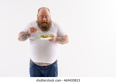 This salad is very tasty. Thick bearded man is eating healthy food with enjoyment. He is looking at plate with surprise and smiling. Isolated and copy space in right side