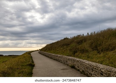 This scenic pathway by the sea, under a cloudy sky, is ideal for peaceful walks and appreciating natures beauty - Powered by Shutterstock