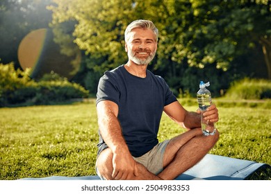 In this serene scene, a man is sitting peacefully in a yoga pose outdoors, surrounded by lush greenery, promoting wellness and encouraging hydration while enjoying the tranquility of nature - Powered by Shutterstock