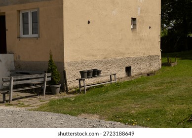 This is a side view of a charming building, showcasing the adjacent garden area that features green grass, inviting wooden benches, vibrant potted plants, and a wellmaintained walkway