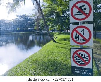This is a sign prohibiting swimming and fishing, this sign is posted near the lake. this sign adds "No swimming" in Indonesian - Shutterstock ID 2270174701