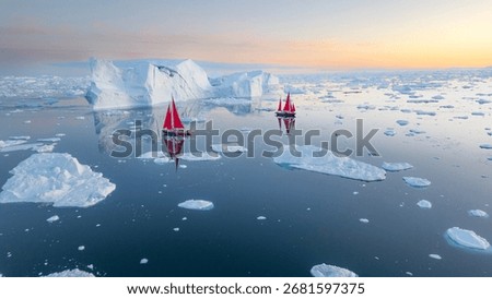 This striking panoramic image captures a tranquil moment in the icy waters of the Arctic. Two small sailboats with vibrant red sails glide past a massive, pristine iceberg and smaller ice floes. The s