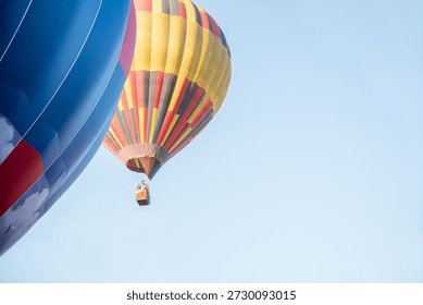 This striking vertical composition features a close-up view of the side of a vibrant blue balloon in the foreground, contrasted against a brilliantly colored yellow and red balloon in the middle ground. The passenger basket is visible as the craft carries travelers over a lush green forest canopy. This high-resolution image captures the spirit of adventure and the beauty of aviation, making it perfect for travel editorials, adventure branding, and inspirational marketing materials.