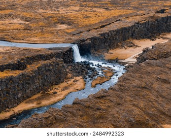 This stunning aerial image captures a waterfall flowing into a winding river amidst Iceland's rugged landscape, showcasing the dramatic beauty of its natural wonders. - Powered by Shutterstock
