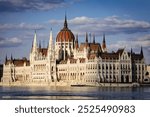 This stunning photo captures the iconic Hungarian Parliament Building in Budapest, showcasing its grand Neo-Gothic architecture along the Danube River, bathed in soft sunlight with a serene water refl