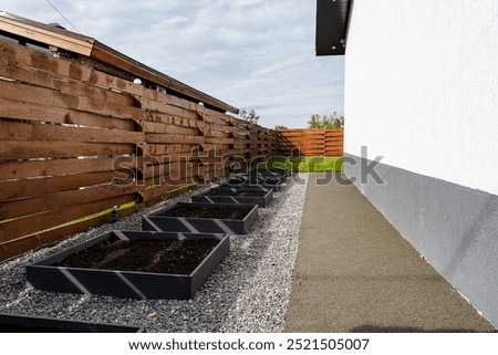 This stylish garden features elevated planters for plant growth, a neat gravel path for easy walking, and a charming wooden fence, ideal for urban gardening and relaxation