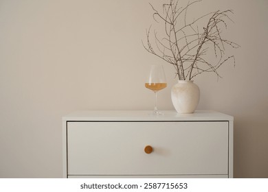 This stylish and highly functional white dresser with glass of wine, ceramic vase with elegant dry branches.
