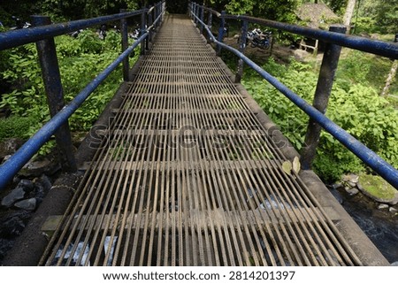 This suspension bridge features a grated metal deck and blue handrails.
