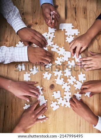 This team isnt easily puzzled. High angle shot of a group of unidentifiable businesspeople building a puzzle together in the office.
