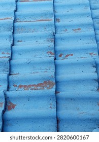 This texture features a weathered, corrugated or overlapping tile surface painted in a faded sky-blue shape.
A vibrant sky blue that is heavily weathered, showing distinct patches where the paint has chipped away to reveal a reddish-brown or terracotta underlayer and raw material beneath.
Arranged in neat, repeating horizontal waves or ridges, characteristic of traditional roofing tiles laid out in vertical interlocking columns.
Strong directional light creates soft highlights along the rounded ridges and deep shadows within the recessed grooves, emphasizing the three dimensional, structured layout.
Rough, chalky, and coarse, marked by minor pits, uneven paint layers, and flaking spots from age and exposure.
Evokes a rustic, industrial, or coastal architectural feel, carrying a sense of history and weathered resilience.