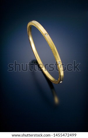 This textured and polished yellow gold bangle bracelet stands on a black reflective background.