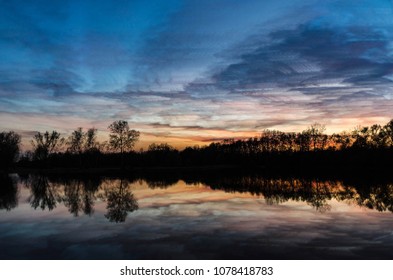 This time stack sunset was created from a bunch of photos. Near the blue and golden hours. Trees and bushes surround the lake, adding a great silhouette and also a warm sunset with blue, reflection