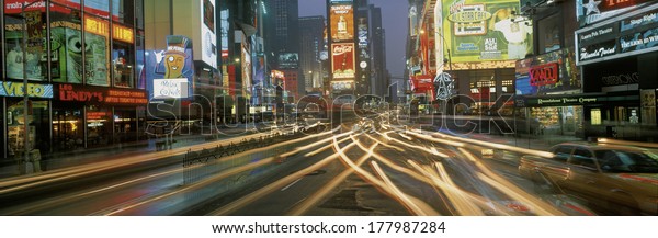 This is Times Square at\
night. There are streaked lights from the cars traveling through\
the square. There are neon lights from the billboards as well as\
signs.