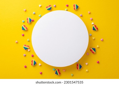 This top view flat lay of LGBT parade accessories on a vibrant yellow background is perfect for celebrating Pride Month, featuring rainbow pin badges, hearts surrounding an empty circle for text or ad