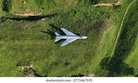 This top-down drone shot features a vintage silver fighter jet on a green meadow. Perfect for military history, aviation, and defense-themed commercial projects.