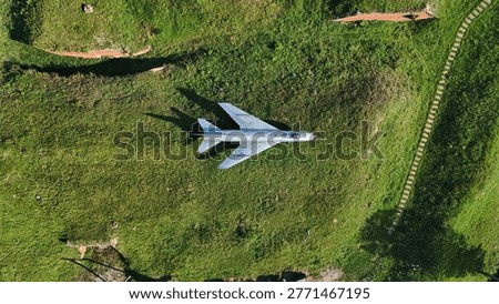 This top-down drone shot features a vintage silver fighter jet on a green meadow. Perfect for military history, aviation, and defense-themed commercial projects.