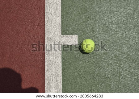 This top-down, high-angle shot captures a bright yellow-green tennis ball resting on the textured surface of an outdoor hardcourt.