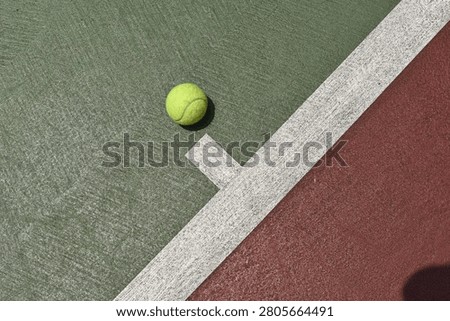 This top-down, high-angle shot captures a bright yellow-green tennis ball resting on the textured surface of an outdoor hardcourt.
