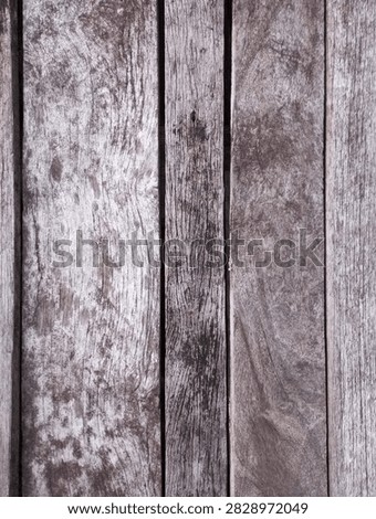 This top-down, vertical close-up captures weathered, textured wooden planks aligned vertically across the frame. The wood exhibits a heavily aged, rustic appearance characterized by prominent grain patterns, natural knots, and deep linear grooving. The color palette consists of cool, desaturated tones, featuring a gradient of light silvery-gray highlights, medium charcoal midtones, and deep brown shadows within the deep gaps between the individual boards. Surface imperfections, including varying degrees of fading, dark weathering spots, and fiber fraying, are highly visible across the material. This natural distressing creates a high-contrast, tactile surface ideal for rustic design backgrounds, weathered decking illustrations, architectural textures, or industrial material studies.