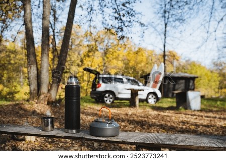 This tranquil camping setup showcases a cozy car, colorful surfboards, and various outdoor gear beautifully arranged among the vibrant autumn foliage and scenery around